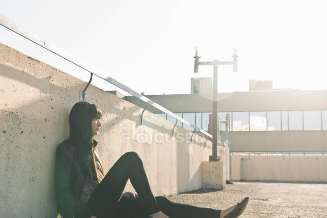 Jeune femme assise sur le toit ensoleillé — Photo de stock