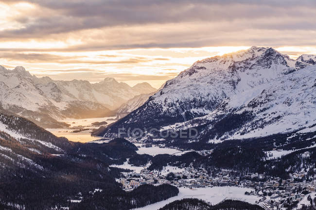 Snowcapped rocky mountains under cloudy sunset sky — Stock Photo