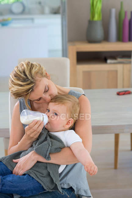 Материнский поцелуй и кормление ребенка бутылкой — стоковое фото