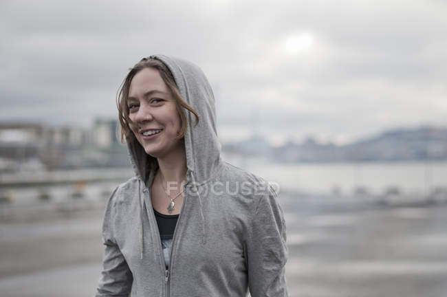 Ritratto di giovane donna che corre indossando una felpa con cappuccio sul bordo del porto ventoso — Foto stock