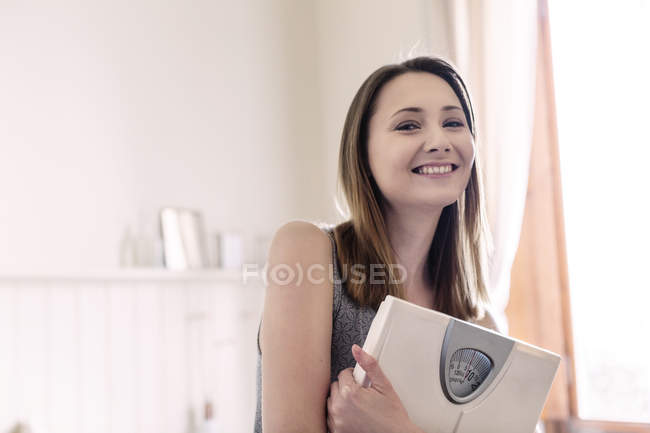 Donna in possesso di bilancia da bagno e guardando la fotocamera sorridente — Foto stock