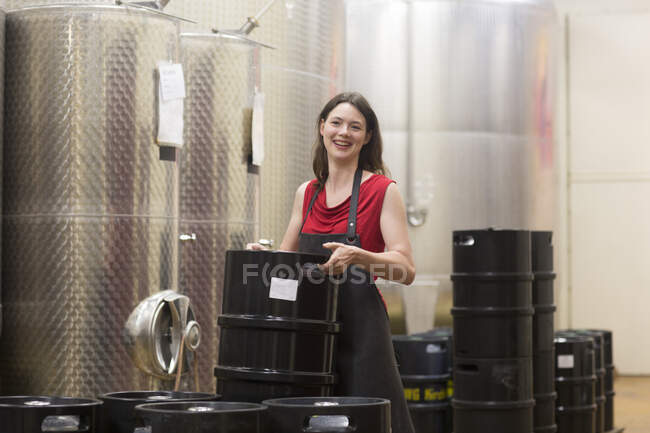 Portrait of young woman in wine cellar next to fermentation tanks, smiling — Stock Photo