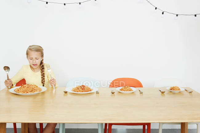Girl sitting at table with spaghetti and three more plates — Stock Photo