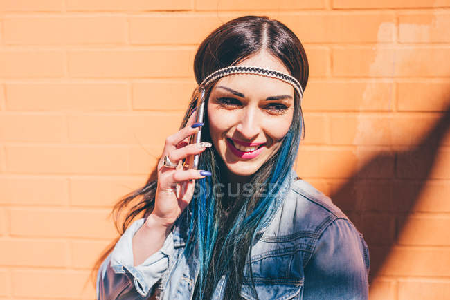 Jeune femme avec des cheveux bleus teints trempés parlant sur smartphone devant un mur orange — Photo de stock