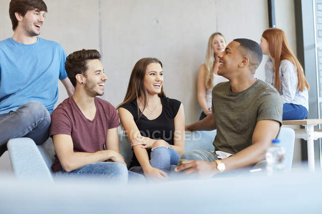 Grupo de jóvenes estudiantes masculinos y femeninos sentados en el sofá del estudio charlando en la universidad de educación superior - foto de stock
