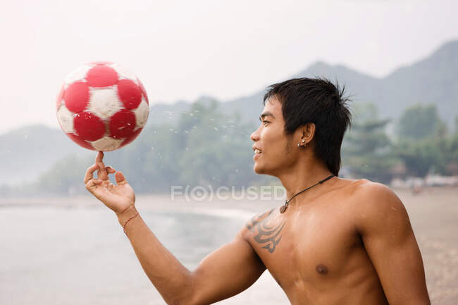 Парень крутит футбол на пальце на пляже — стоковое фото