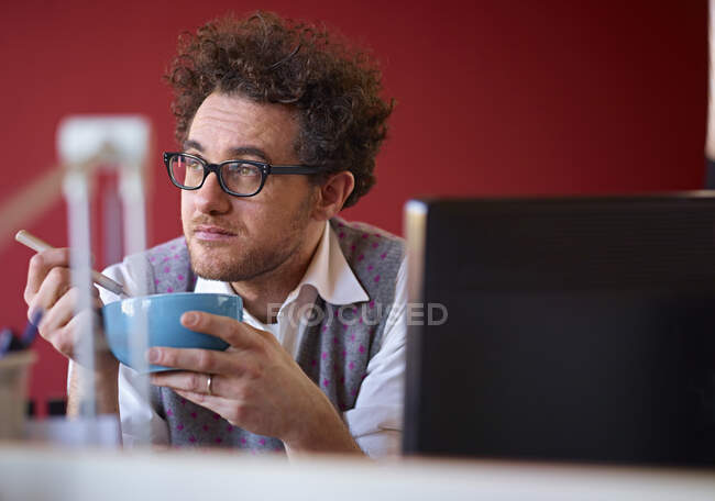 Office worker eating breakfast cereal at desk — Stock Photo