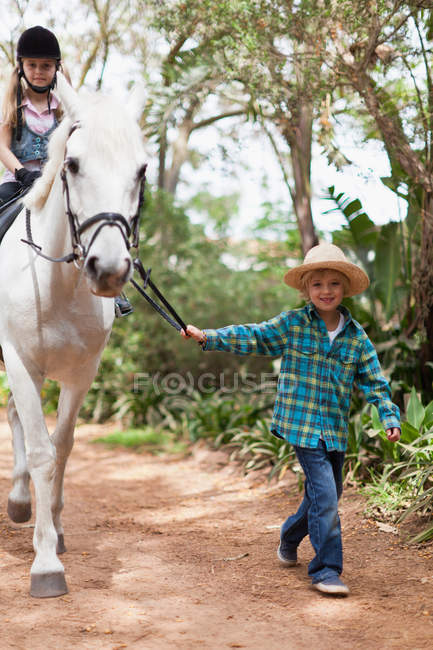 Menino andando com menina montando a cavalo, foco em primeiro plano — Fotografia de Stock