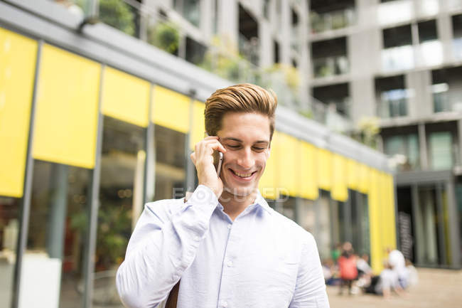 Young businessman talking on smartphone outside office, London, UK — Stock Photo