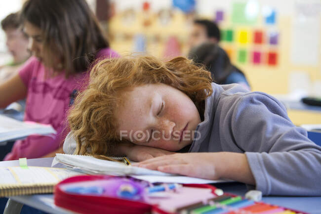 Primary schoolgirl asleep at desk in classroom — Stock Photo