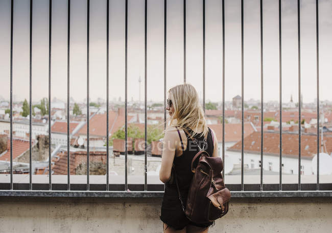Jeune femme regardant à travers les balustrades, vue sur les toits, vue arrière — Photo de stock