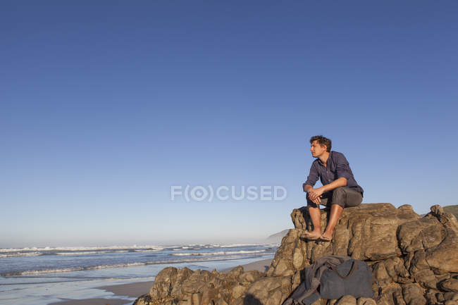 Hombre sentado en la roca a la orilla del mar - foto de stock