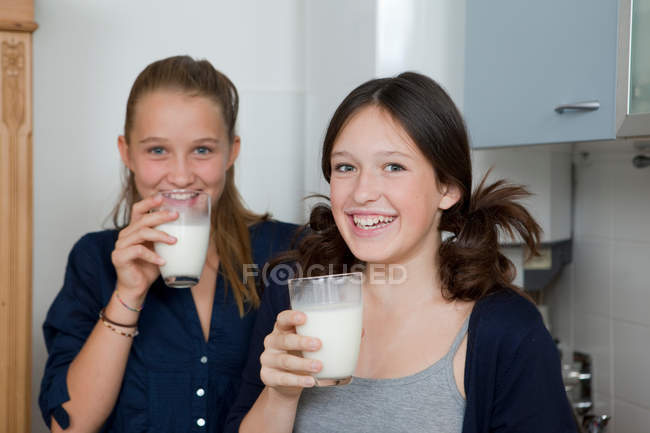 Filles souriantes boire du lait dans la cuisine, se concentrer sur le premier plan — Photo de stock