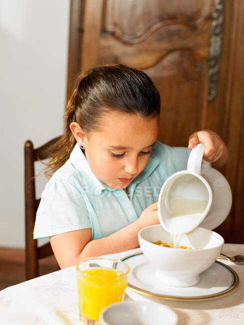 Chica vertiendo leche en el cereal - foto de stock