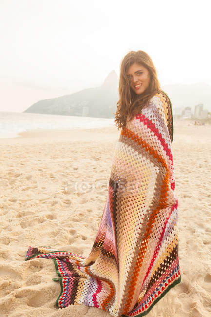 Mujer joven envuelta en manta, Playa de Ipanema, Río de Janeiro, Brasil - foto de stock