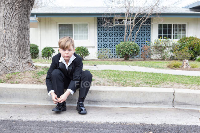 Niño de traje sentado en la calle suburbana - foto de stock