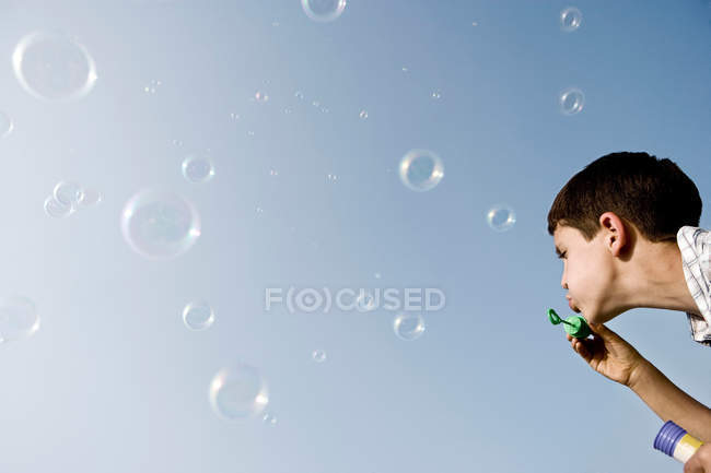 Menino soprando bolhas contra o céu azul — Fotografia de Stock