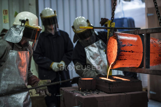 Trabajadores de fundición masculina vertiendo crisol de bronce en fundición de bronce - foto de stock