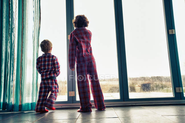 Vue arrière des garçons en pyjama regardant par la fenêtre — Photo de stock