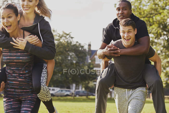 Homens e mulheres se divertindo treinando no parque, tendo piggy volta corrida — Fotografia de Stock