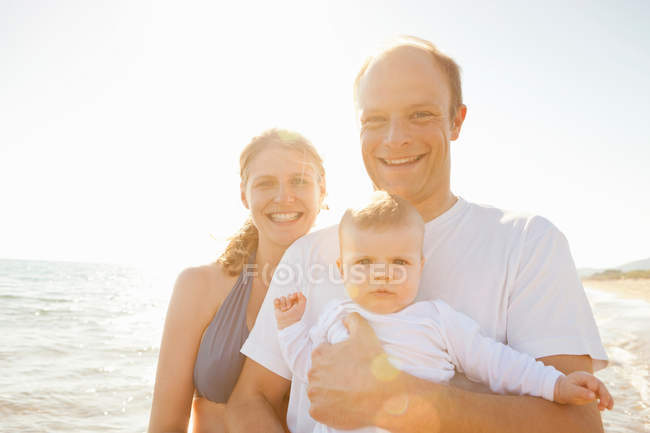 Famiglia sorridente in piedi sulla spiaggia — Foto stock