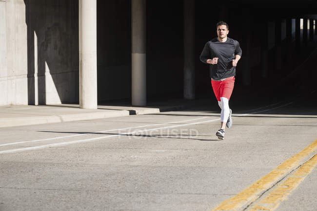 Young male runner running from city underpass — Stock Photo