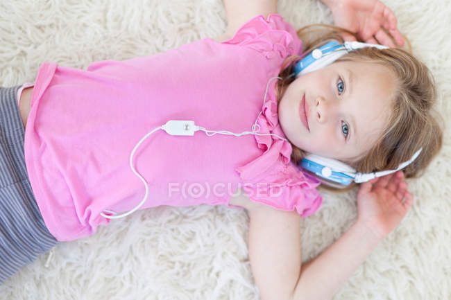 Chica escuchando auriculares en la alfombra, vista de ángulo alto - foto de stock