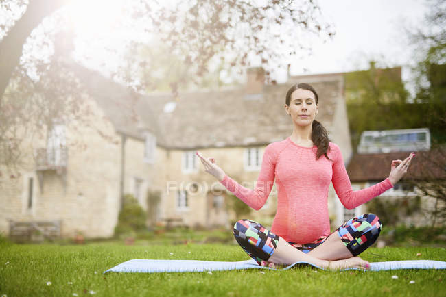 Беременная женщина сидит на улице, в позе йоги — стоковое фото