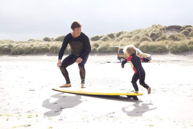 Батько і син з дошкою для серфінгу на пляжі — стокове фото