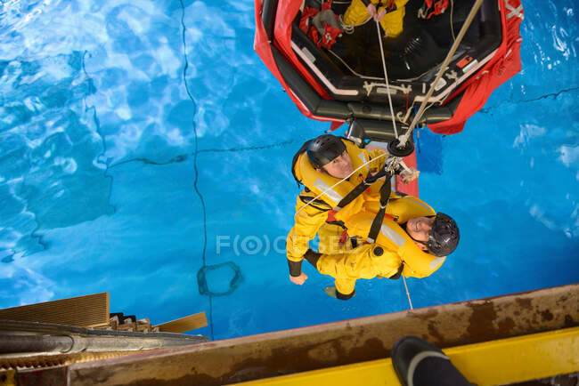 Offshore oil workers hoisted from raft in sea ditching survival training in pool facility — Stock Photo
