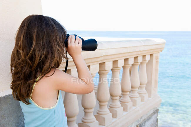 Girl with binoculars looking out to sea — Stock Photo