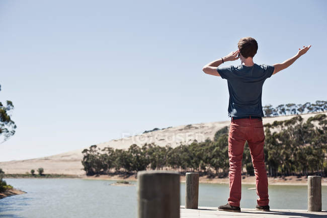 Rear view of young man on mobile phone, overlooking lake scene — Stock Photo