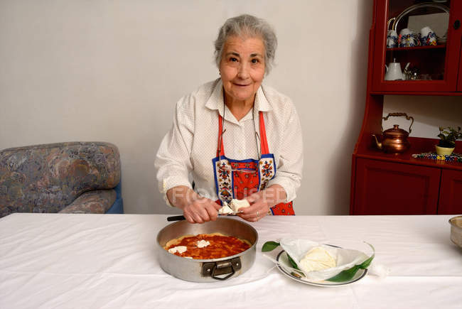 Ältere Frau schneidet Käse für Pizza — Stockfoto