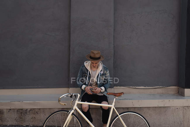 Молодий чоловік сидів на стіні, велосипед перед ним, за допомогою смартфона — стокове фото