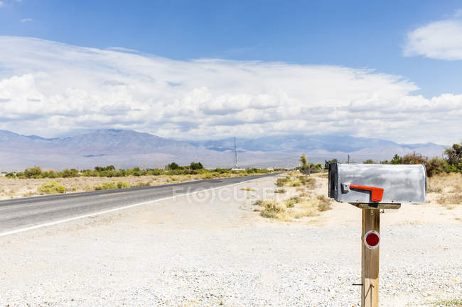 Поштова скринька на сільській дорозі під блакитним хмарним небом — стокове фото