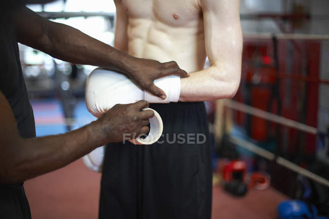 Coach helping boxer put on gloves, mid section — Stock Photo