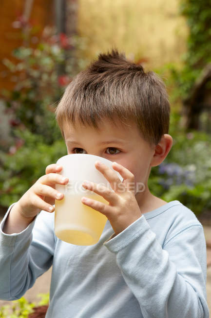 Niño bebiendo jugo en el jardín - foto de stock
