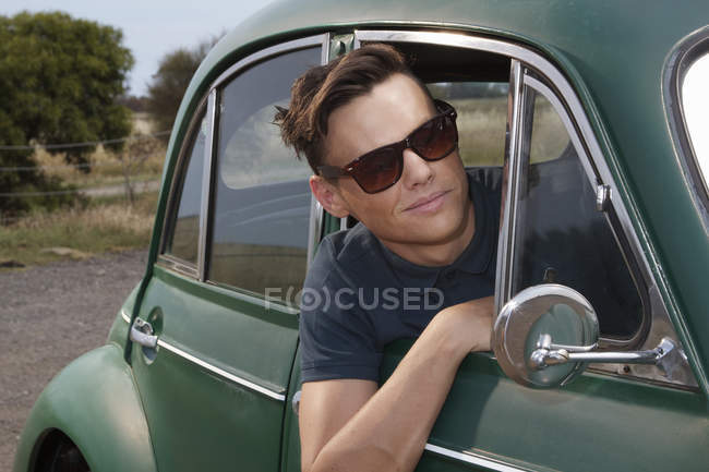 Young man leaning out of vintage morris minor — Stock Photo