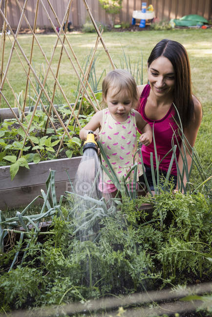 Mutter und Tochter im Garten, Pflanzen mit Schlauch gießen — Stockfoto