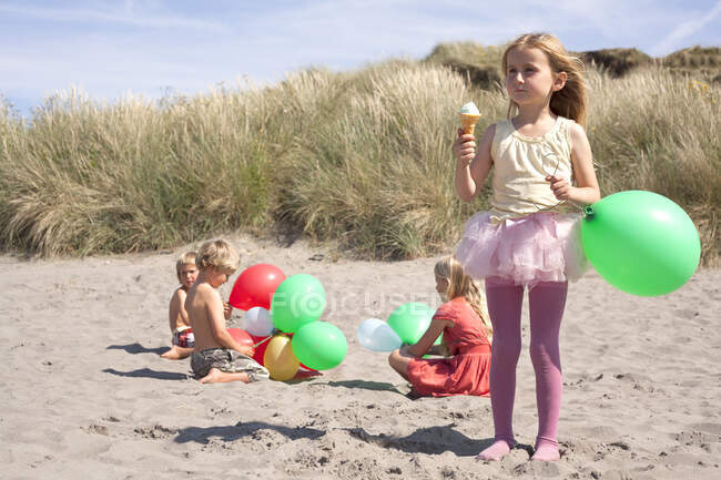 Девушка, держащая воздушный шар, ест мороженое на пляже, Уэльс, Великобритания — стоковое фото