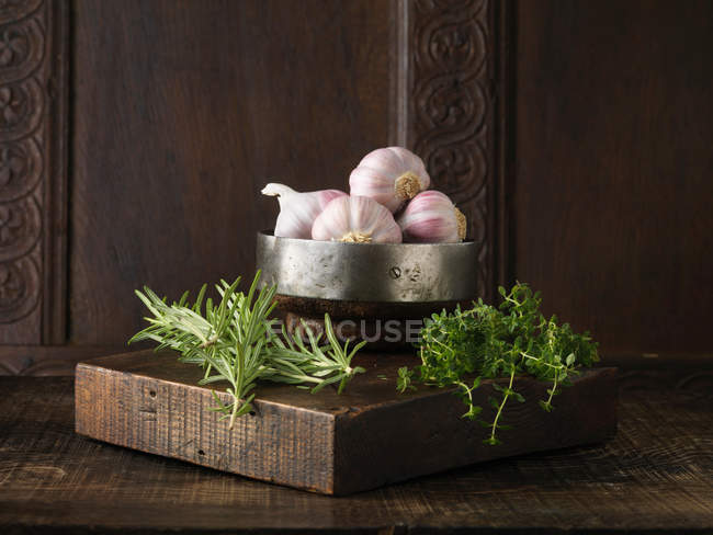Garlic, rosemary and thyme on rustic wooden board — Stock Photo