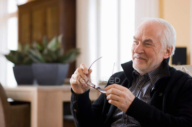 Old man holding pair of glasses smiling — Stock Photo
