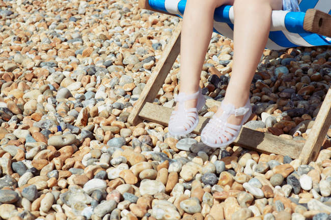 Enfant avec sandales en plastique sur chaise longue de plage — Photo de stock