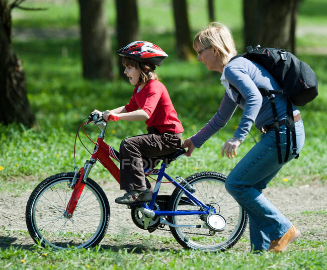 Mother pushing son on bicycle in park — Stock Photo