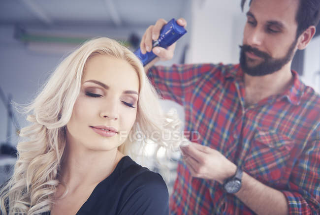Male hairdresser putting hairspray on model for photo shoot — Stock Photo