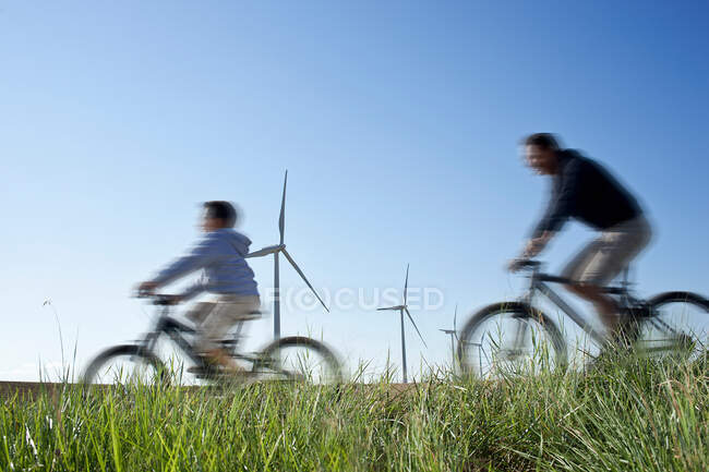 Padre e hijo pasando en bicicleta por un parque eólico - foto de stock
