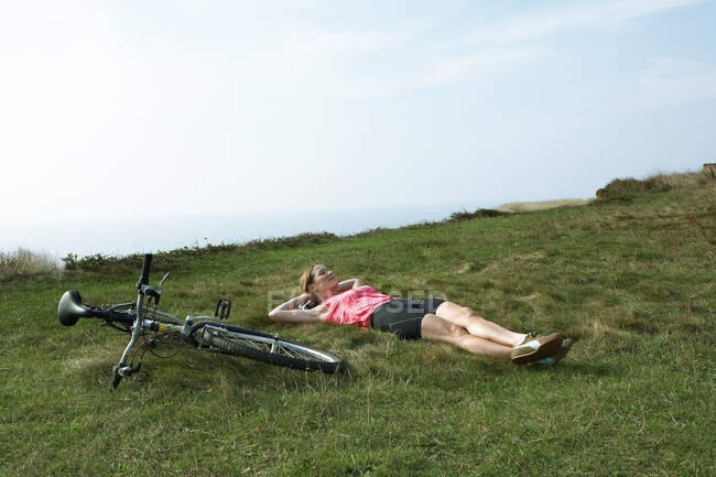 Une femme repose sur l'herbe par son vélo — Photo de stock