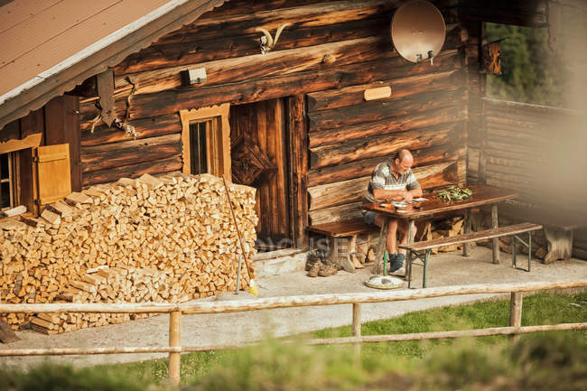 Homem lendo no alpendre da cabine de madeira — Fotografia de Stock