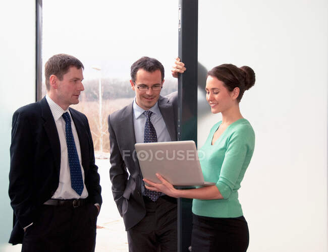 Три колеги говорять, жінка тримає ноутбук — стокове фото