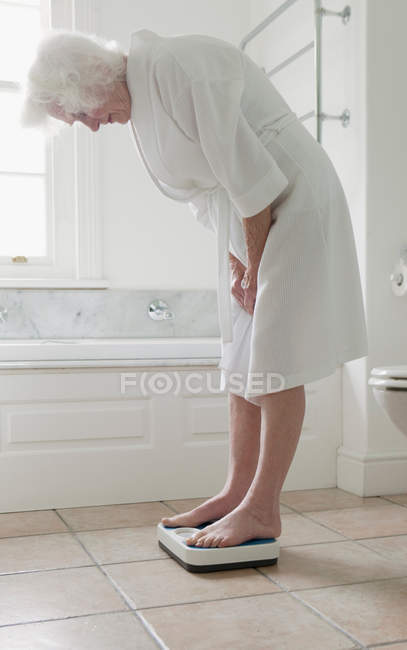 Femme plus âgée se pesant dans la salle de bain — Photo de stock